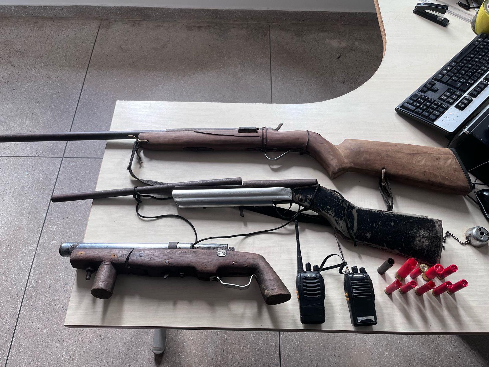 A imagem em destaque mostra o material apreendido com os suspeitos: três armas de fabricação caseira, munições e dois rádios comunicadores.